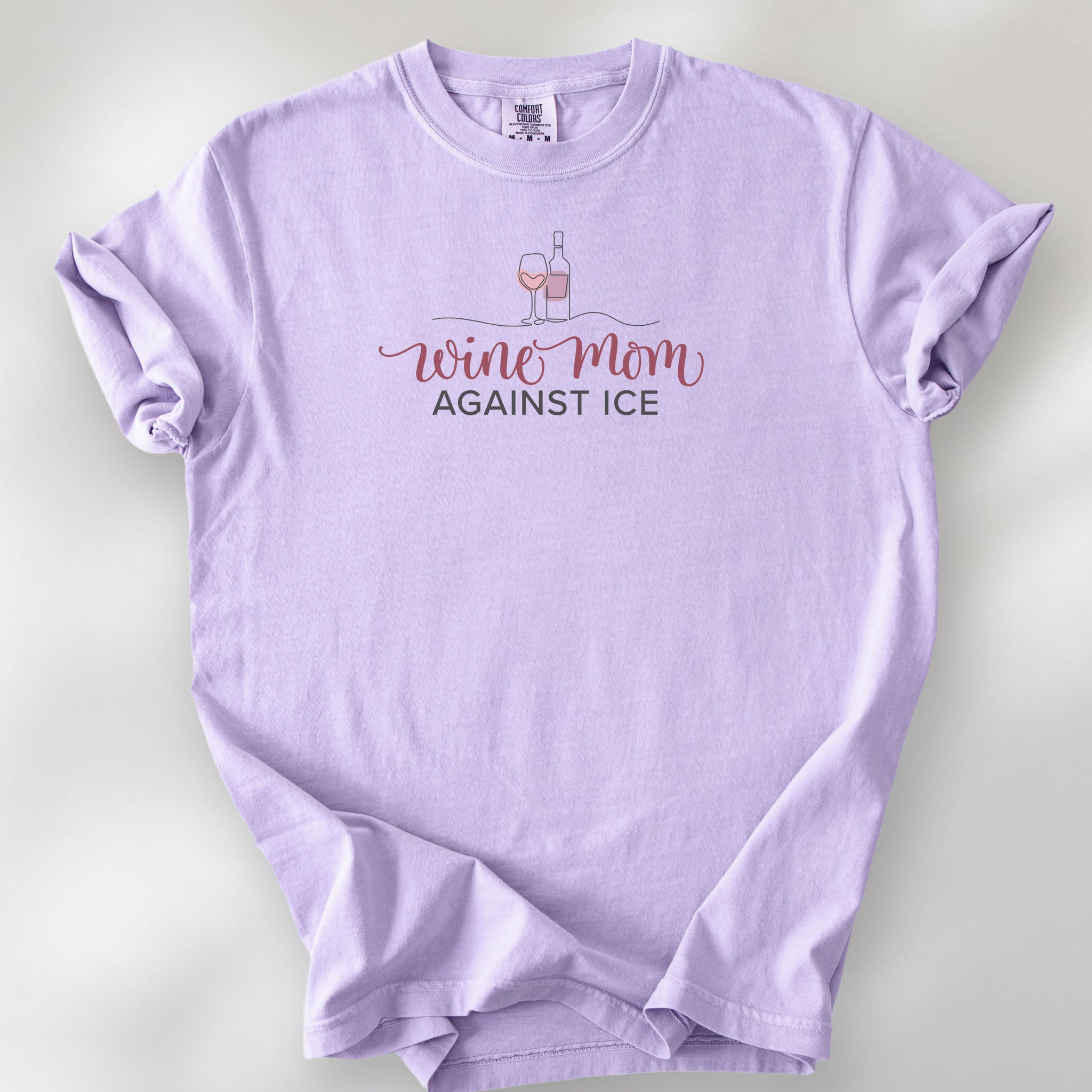 Orchid t-shirt featuring the text “Wine Mom Against ICE” with a minimalist illustration of a wine bottle and glass above the lettering.