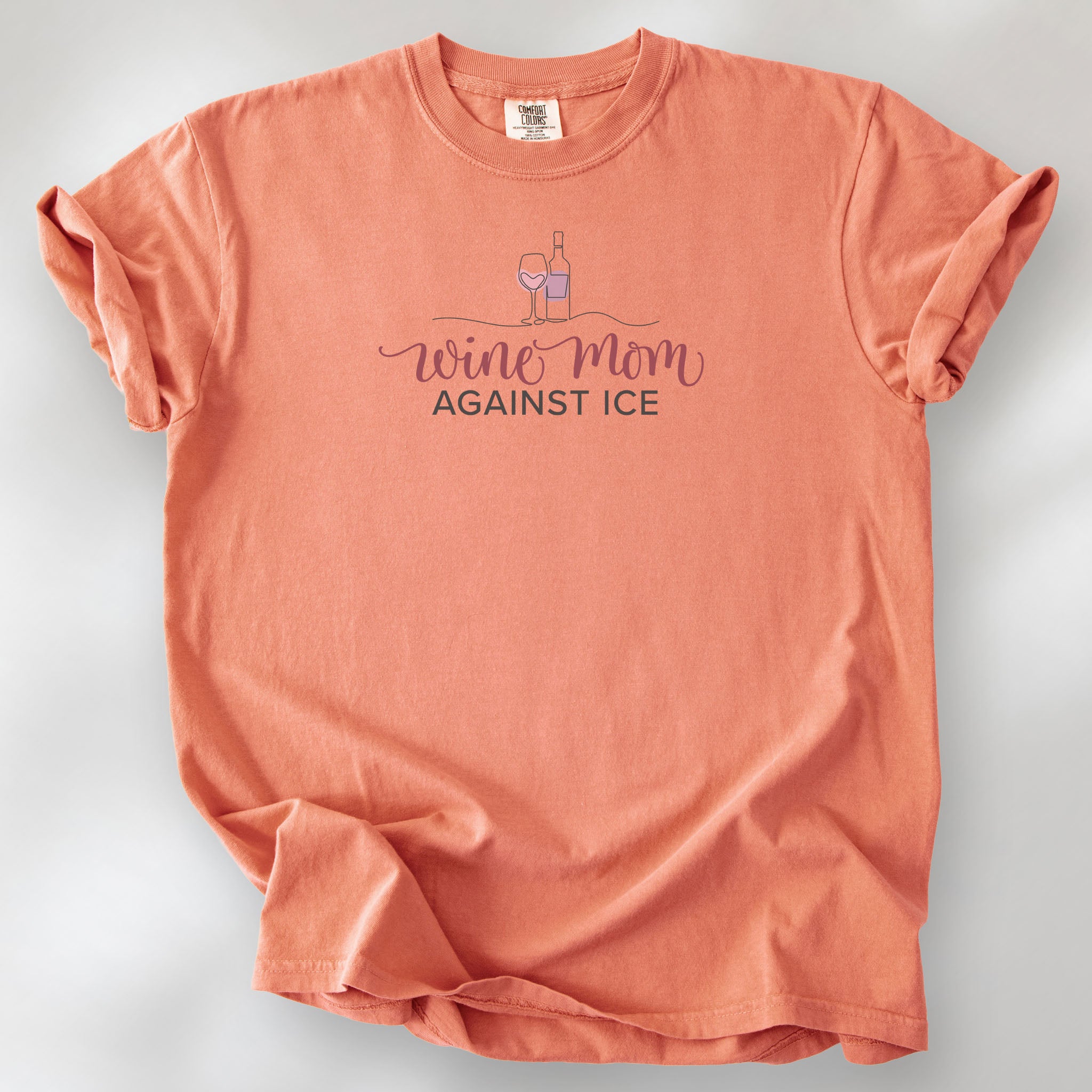 Terracotta t-shirt featuring the text “Wine Mom Against ICE” with a minimalist illustration of a wine bottle and glass above the lettering.
