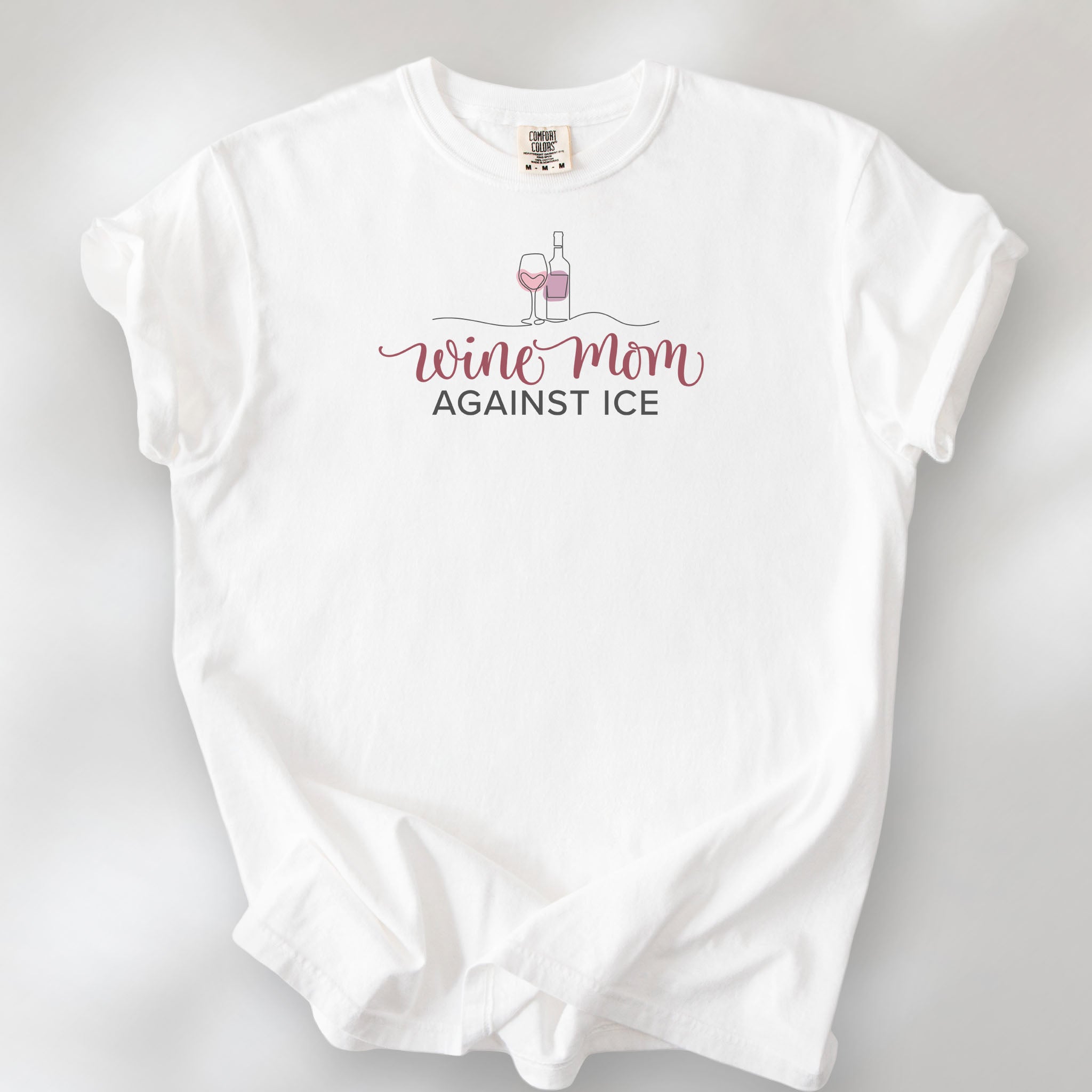 White t-shirt featuring the text “Wine Mom Against ICE” with a minimalist illustration of a wine bottle and glass above the lettering.