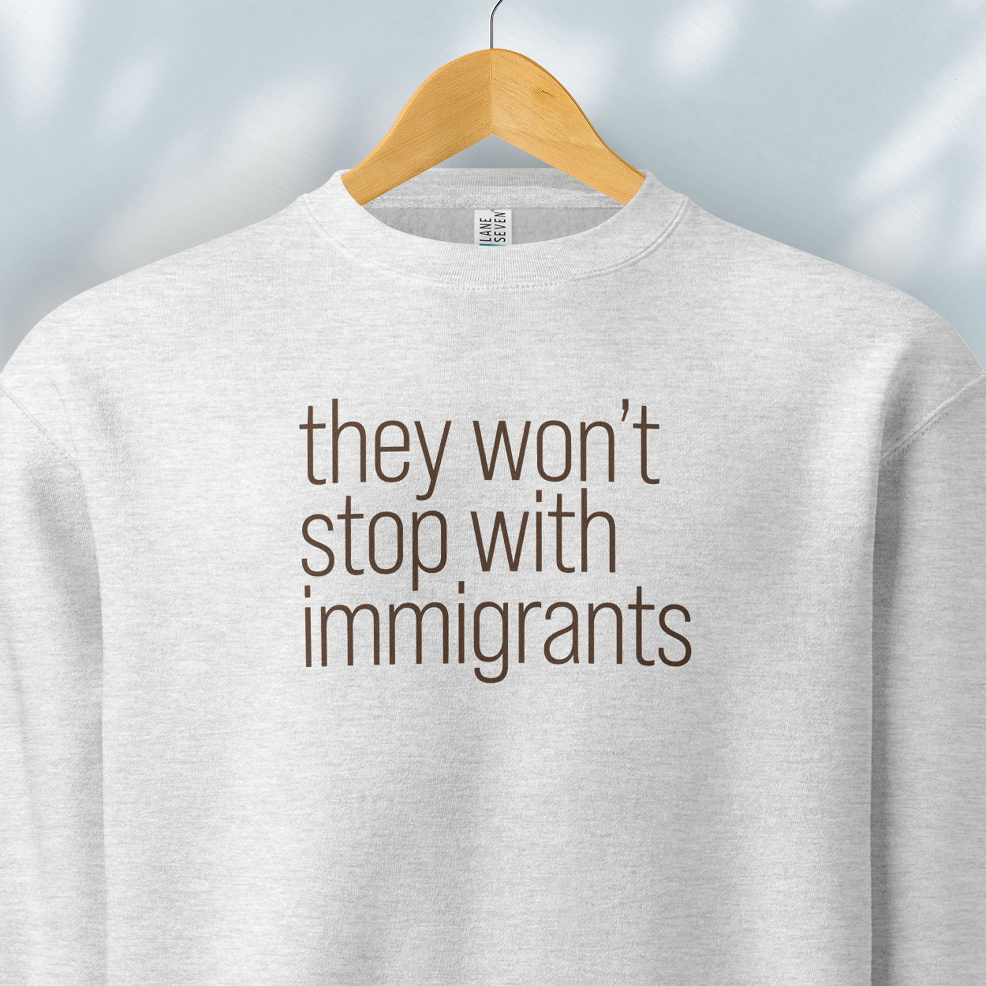 Hanging grey sweatshirt with anti-ICE, anti-trump, anti-tyranny message that reads "they won't stop with immigrants."