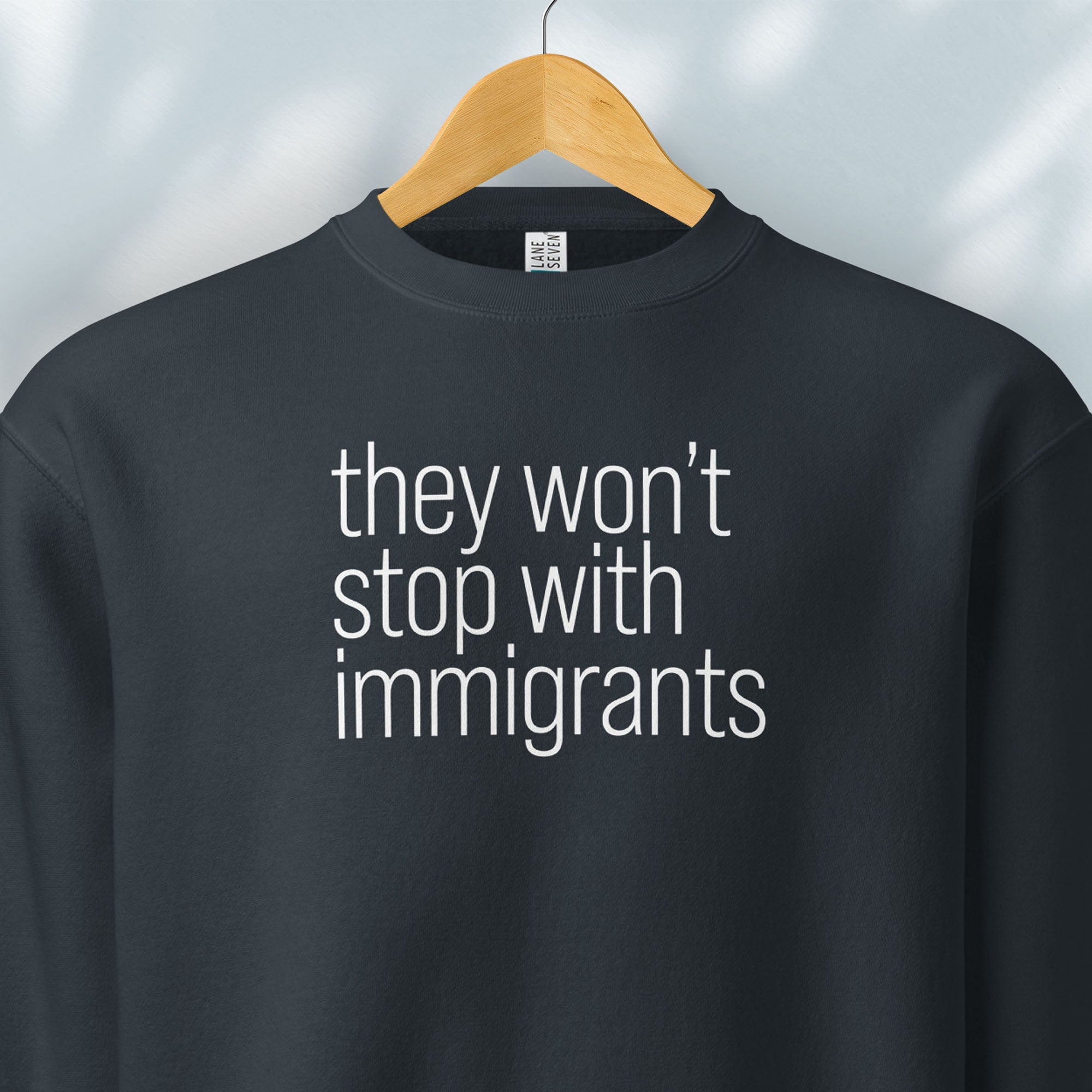 Hanging navy sweatshirt with anti-ICE, anti-trump, anti-tyranny message that reads "they won't stop with immigrants."