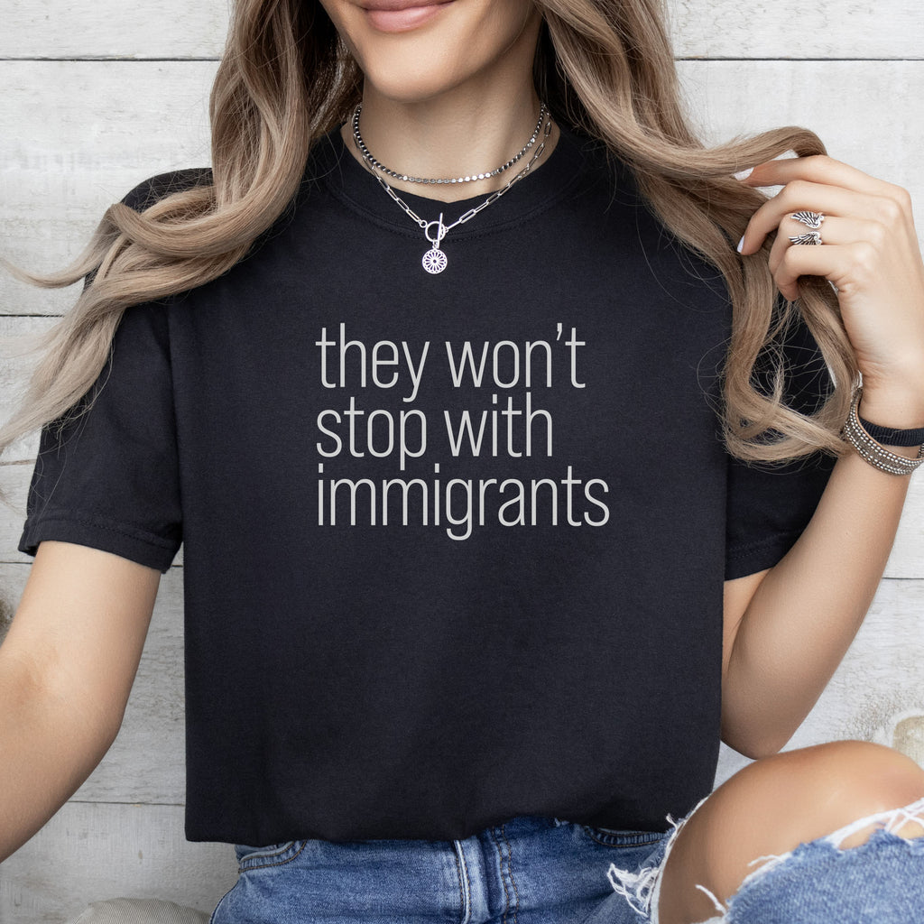 Female model wearing black shirt with minimalist text that reads "they won't stop with immigrants."