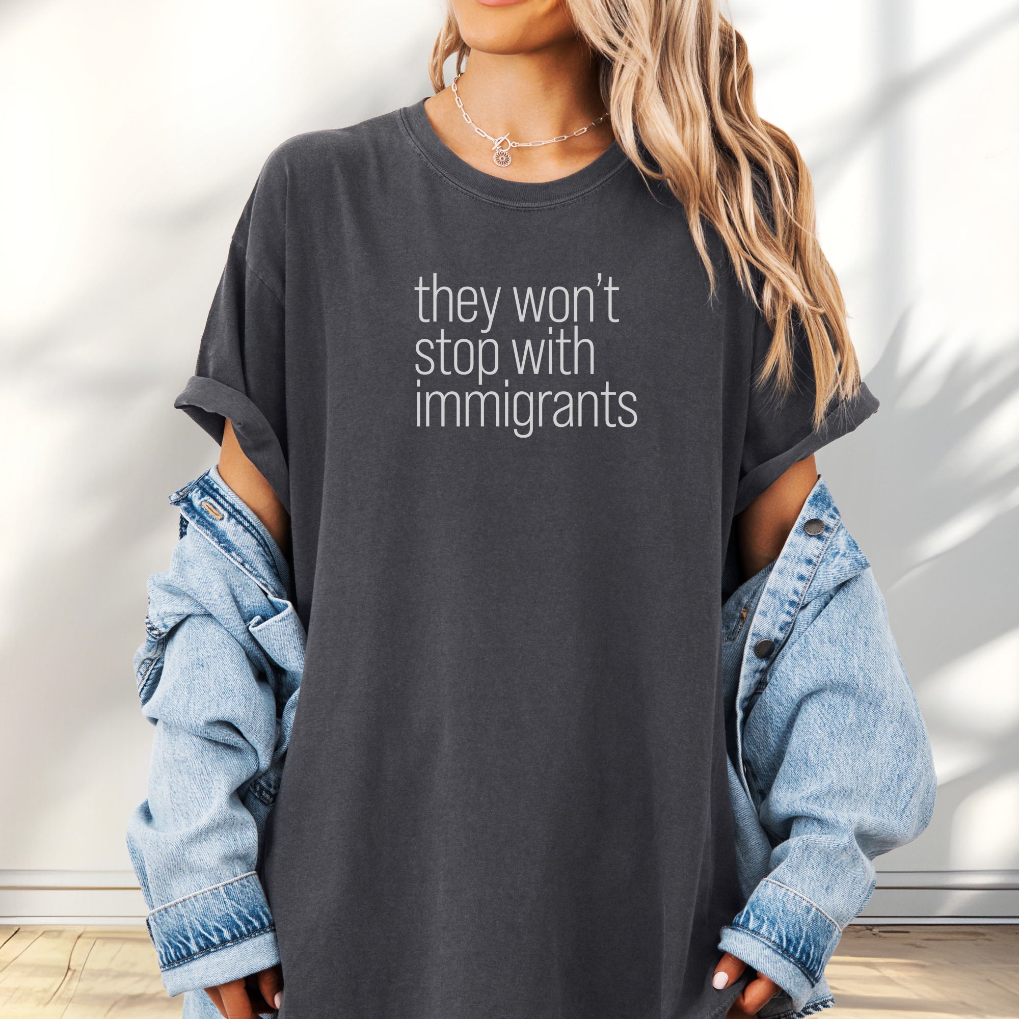 Female model wearing oversized pepper shirt with minimalist text that reads "they won't stop with immigrants."