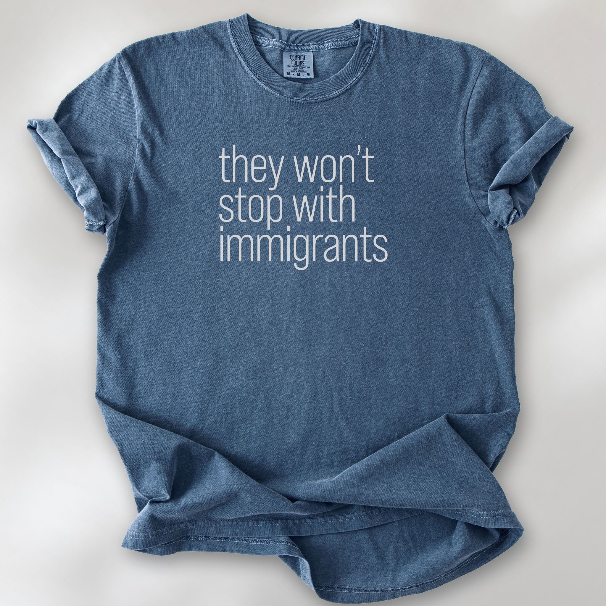 Denim shirt with minimalist text that reads "they won't stop with immigrants."